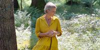 eine Frau in gelbem Kleid steht im Wald neben einem Baum